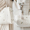 A close-up of a cream quilted diaper bag with subtle floral embroidery shown against a light background.