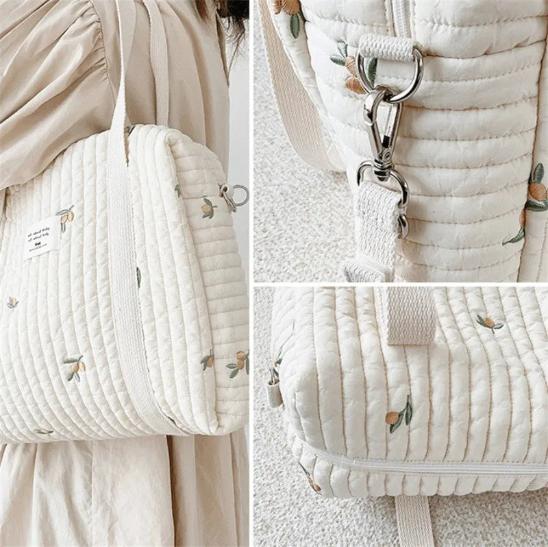 A close-up of a cream quilted diaper bag with subtle floral embroidery shown against a light background.