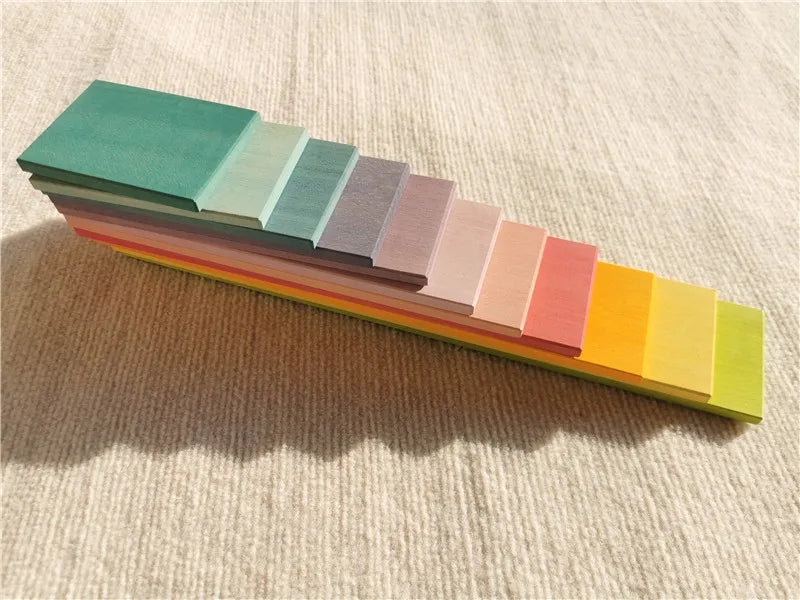 A set of pastel wooden stacking blocks arranged in a horizontal gradient of colors.