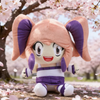 A soft collectible plush doll of Lyna with pink hair and purple accents sitting outdoors among cherry blossoms.