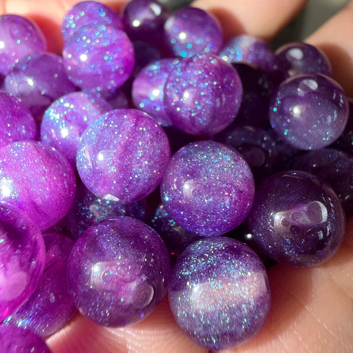 A handful of purple resin spacer beads with a starry sky effect for jewelry making