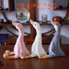 Three plush toys of long-necked geese in pink, white, and gray colors displayed on a wooden surface.