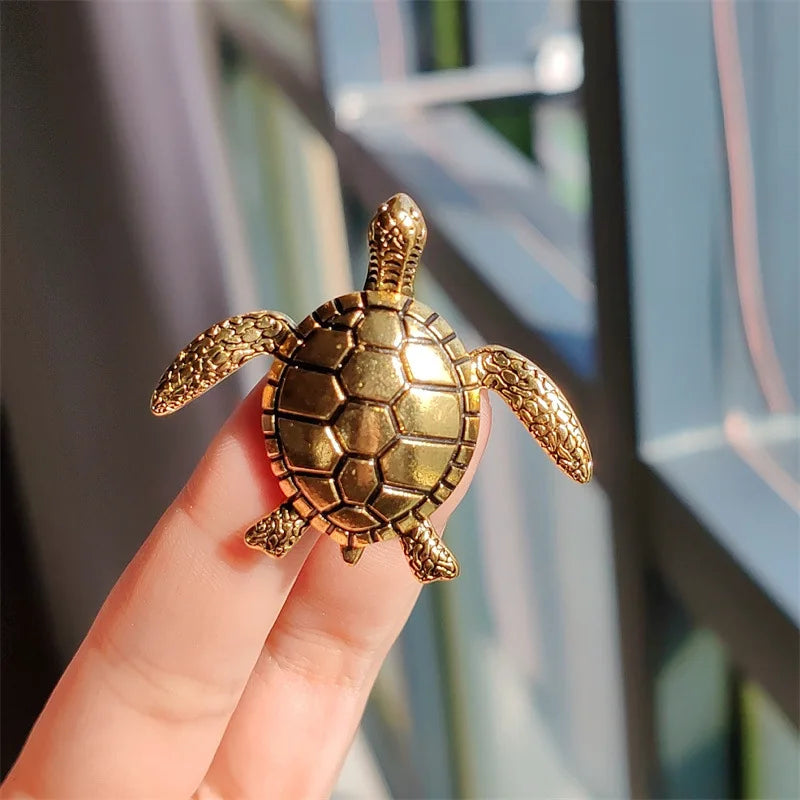 A golden rhinestone turtle brooch pin held by a hand against a blurred window background.