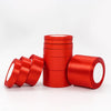 A stack of red satin ribbon rolls for gift wrapping and crafts, displayed on a white surface.