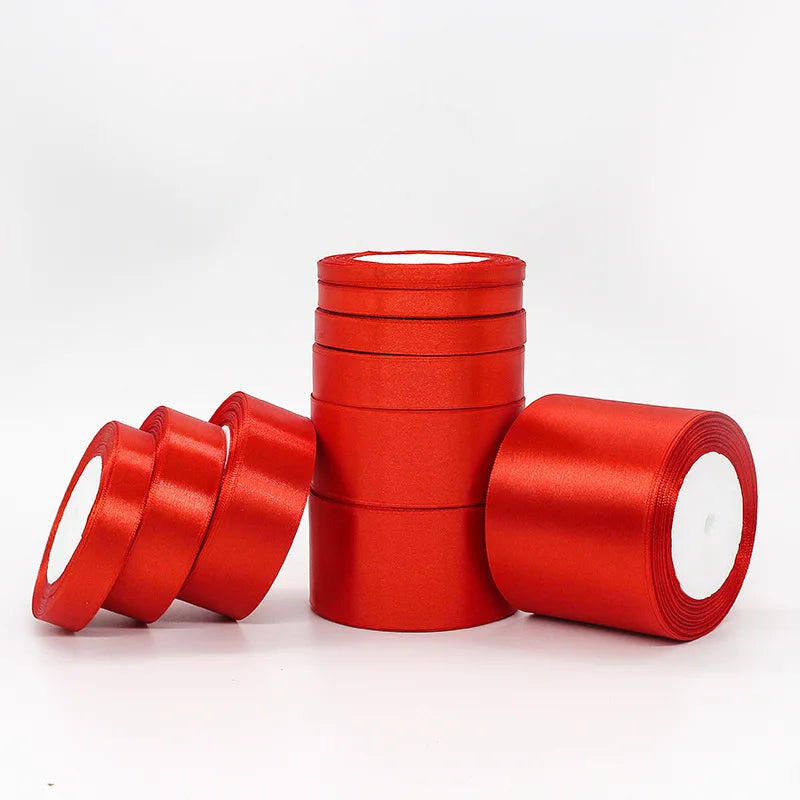 A stack of red satin ribbon rolls for gift wrapping and crafts, displayed on a white surface.