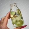 A hand holds a clear glass bottle filled with green liquid and sliced cucumbers, used as a sensory toy.