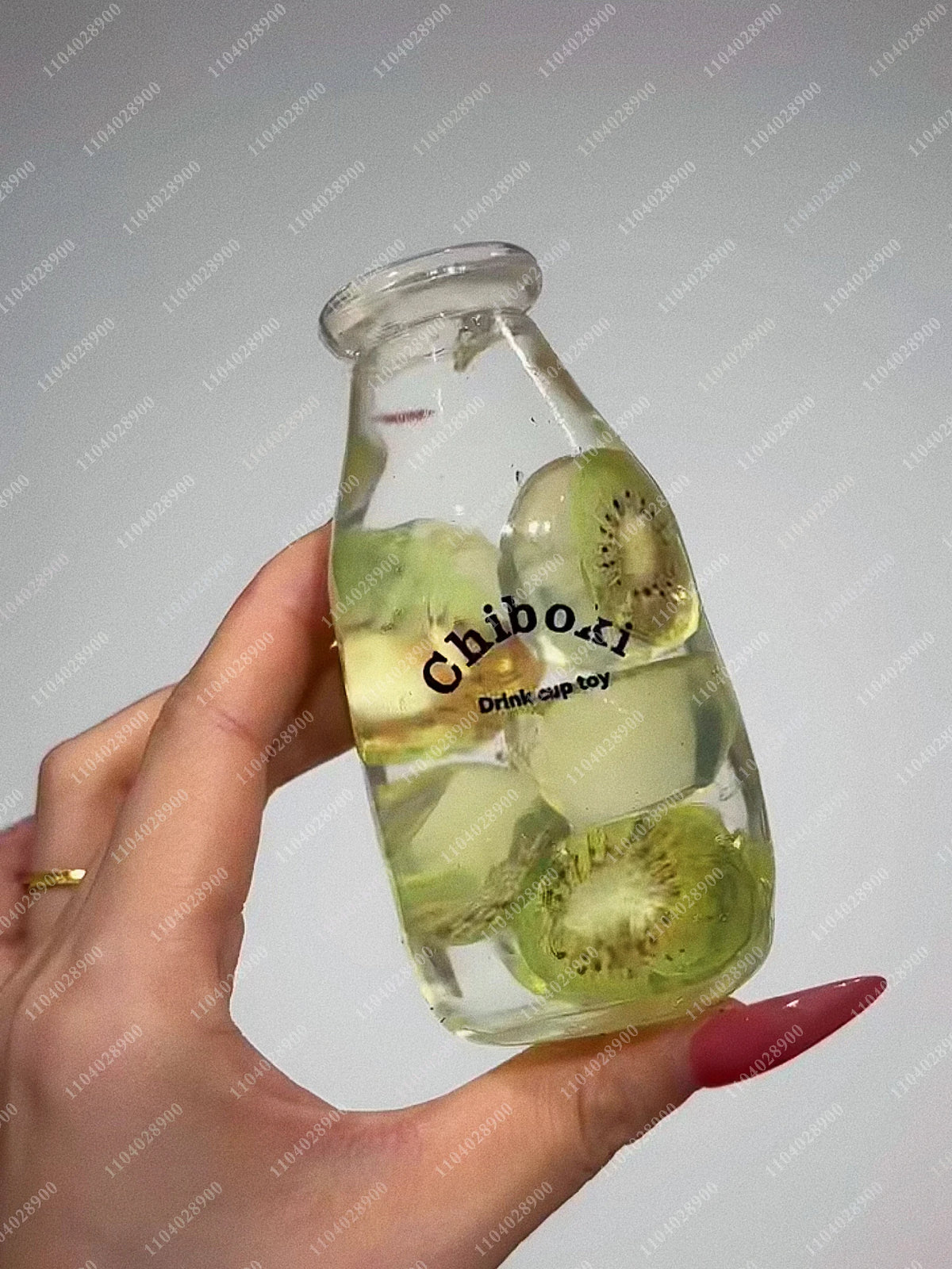 A hand holds a clear glass bottle filled with green liquid and sliced cucumbers, used as a sensory toy.