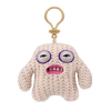 A light pink, fuzzy plush monster keychain with large purple eyes and a pink mouth, attached to a gold-colored loop.