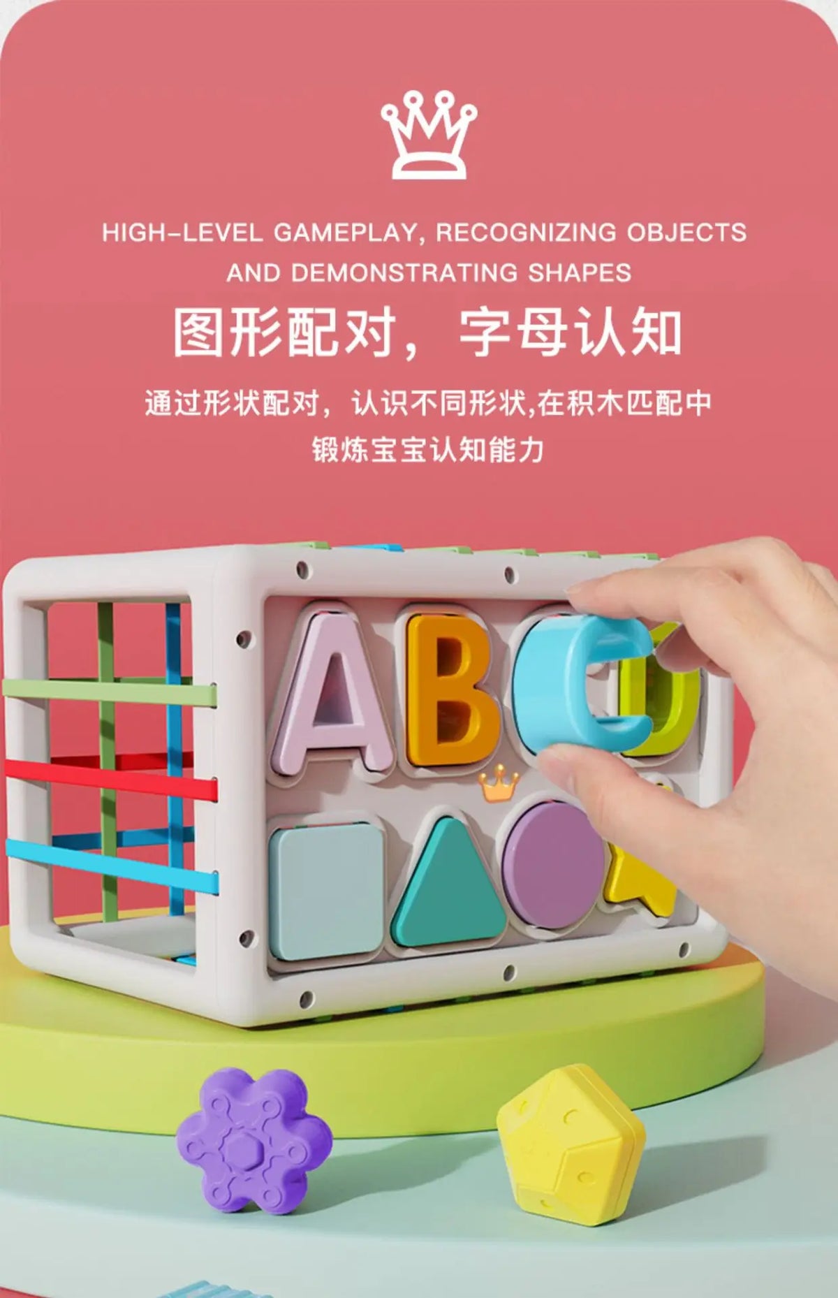 A hand holds a white Montessori shape sorting cube with colorful plastic shapes and elastic bands on a green surface.