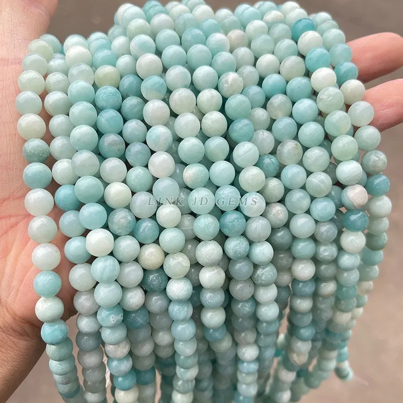 A hand holds a string of light blue and white natural amazonite beads for jewelry making