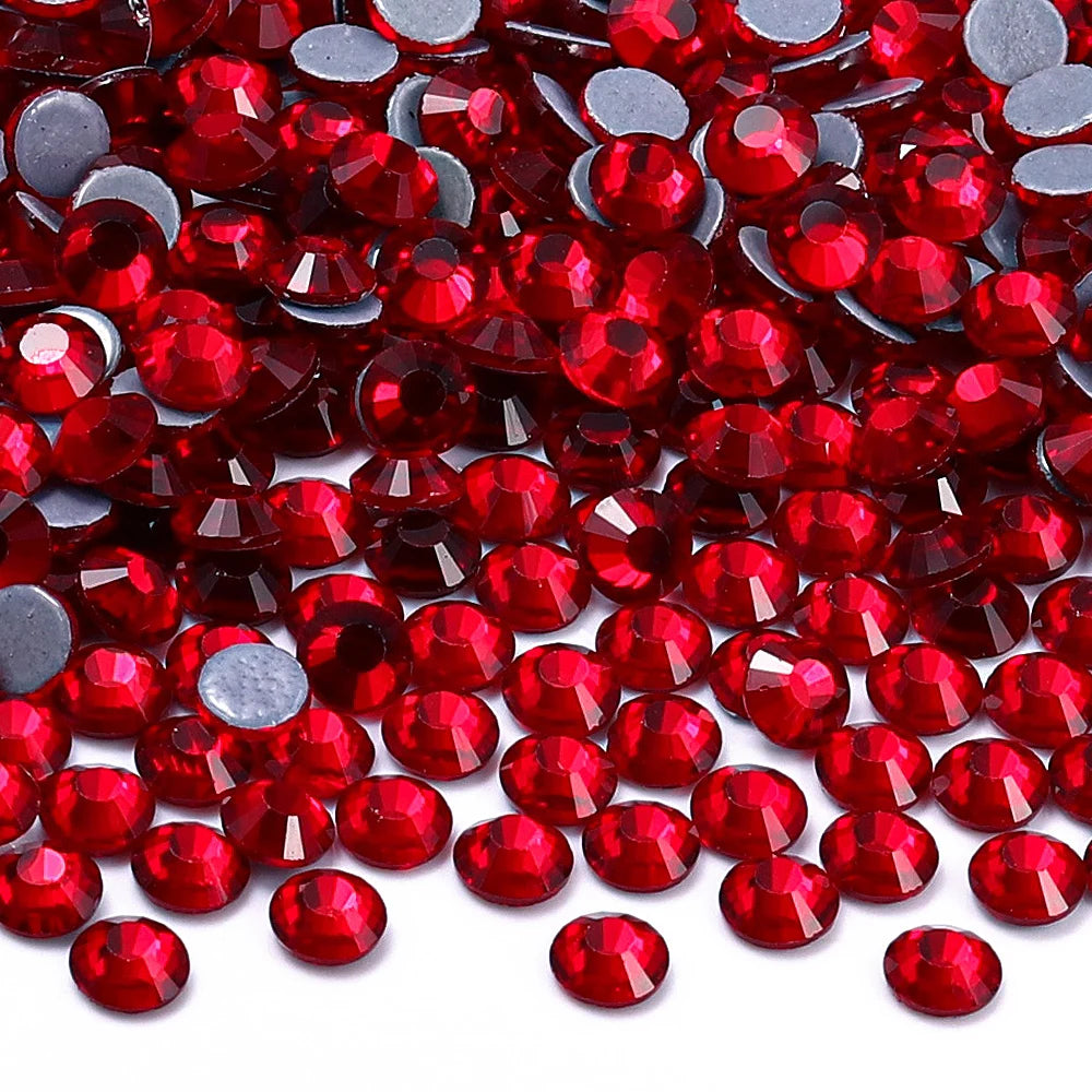 A close-up view of small, faceted red glass crystal rhinestones scattered on a white surface.