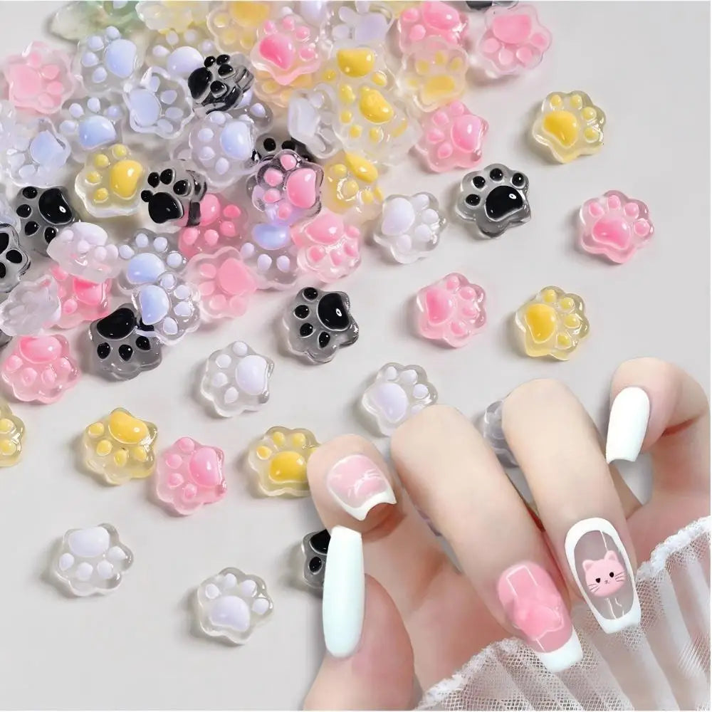A hand displays a variety of luminous cat paw nail art charms for DIY crafts.