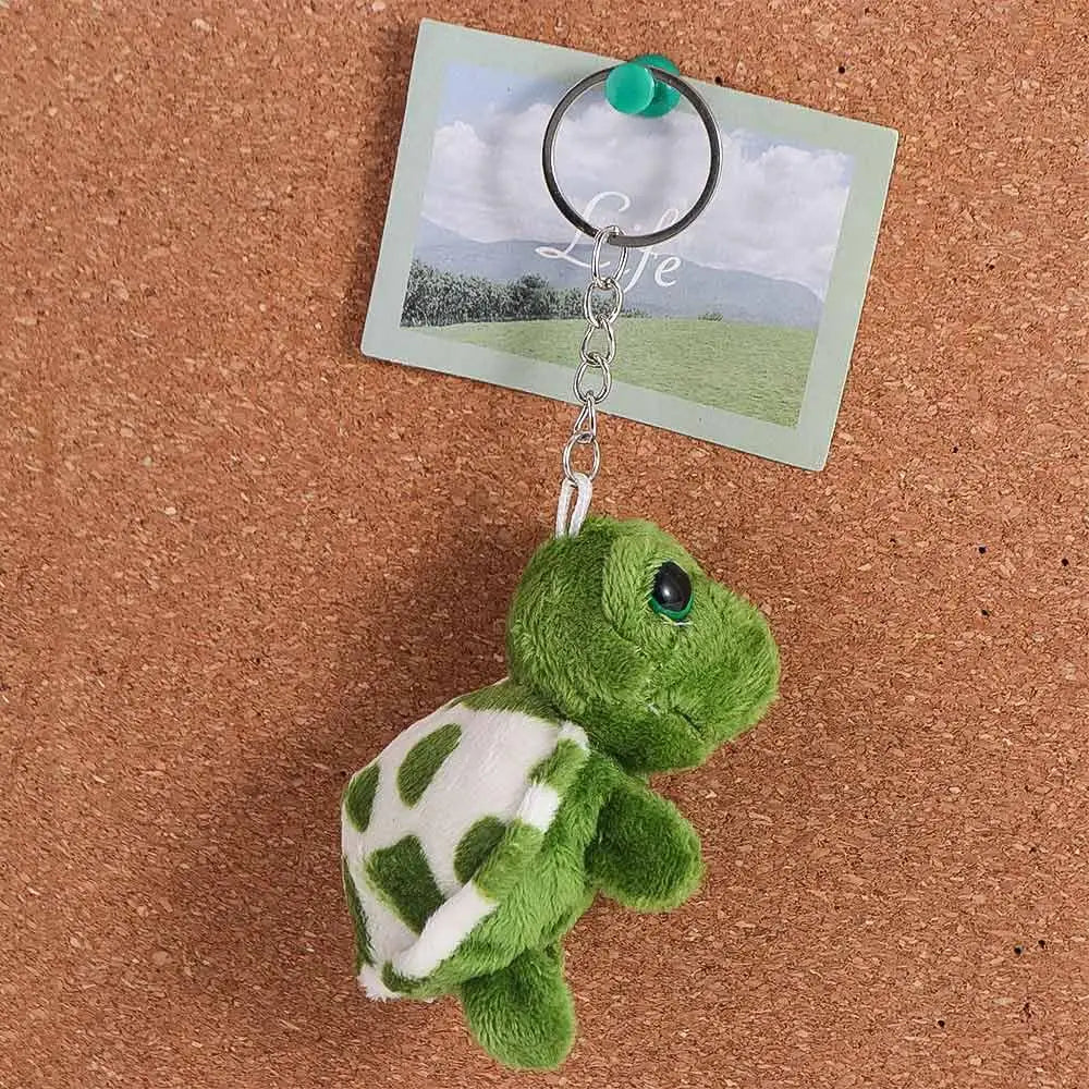 A green turtle plush toy attached to a silver keyring charm on a light green card.