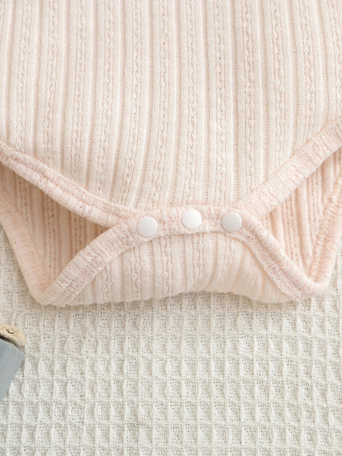 A light pink knitted baby romper and pants set with a gathered front detail.