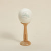 A white, smooth ball decorated with light green leaves rests on a wooden stand.