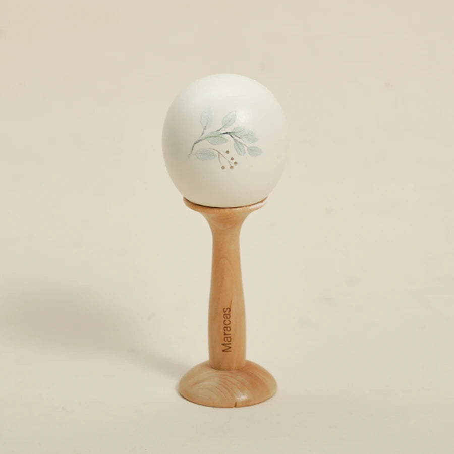 A white, smooth ball decorated with light green leaves rests on a wooden stand.