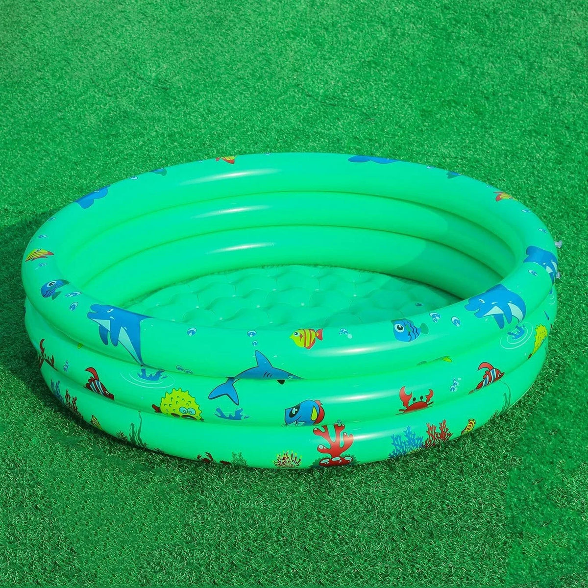 A bright green inflatable kids play pool with a colorful cartoon design resting on green turf.