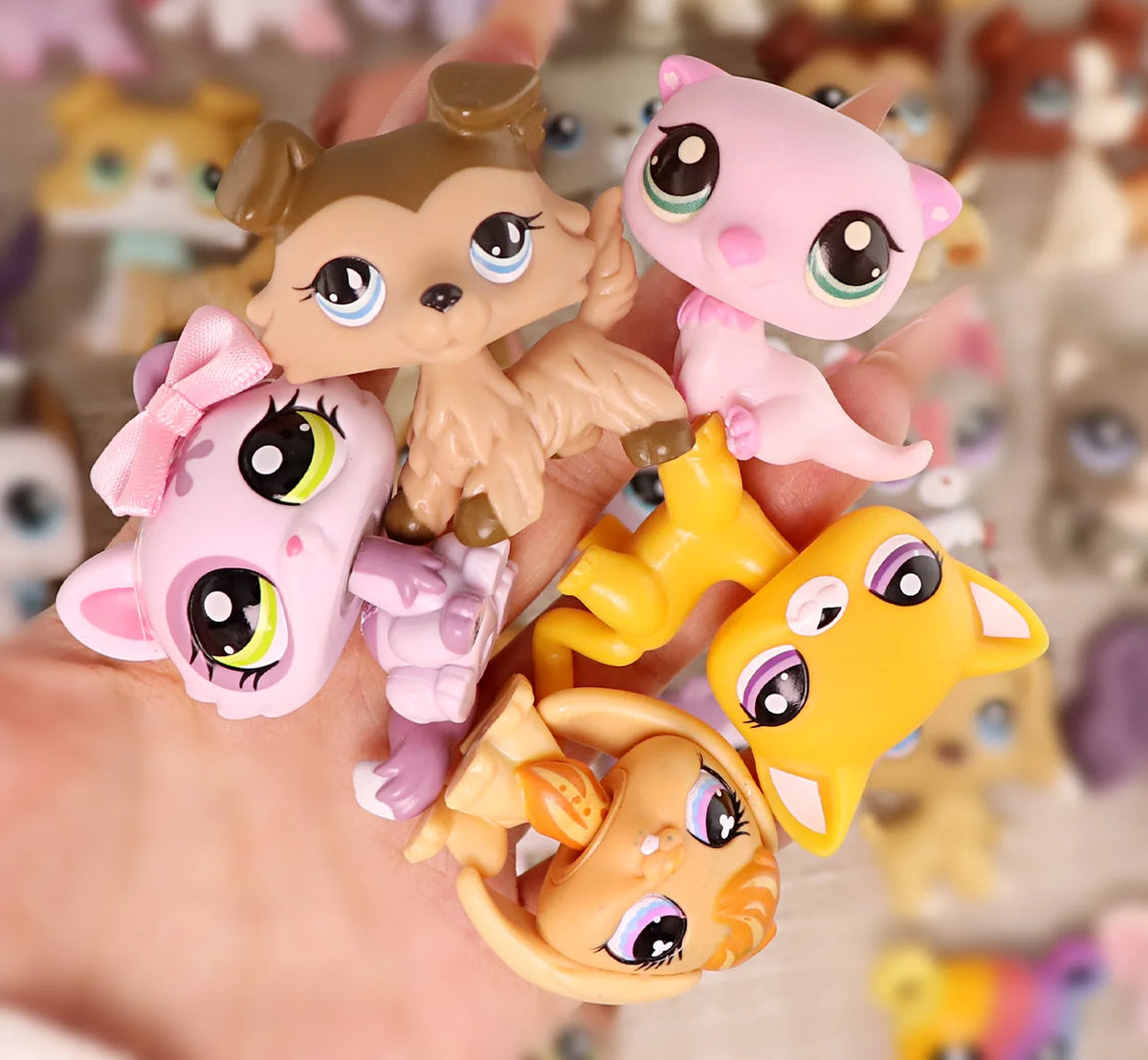 A hand holds a set of miniature pet animal figures in various shades of pink and yellow.