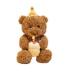 A brown teddy bear plush toy wearing a gold star hat and holding a birthday cake.