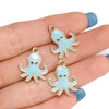 Three light blue enamel marine life charms with gold-colored jump rings displayed on a hand.