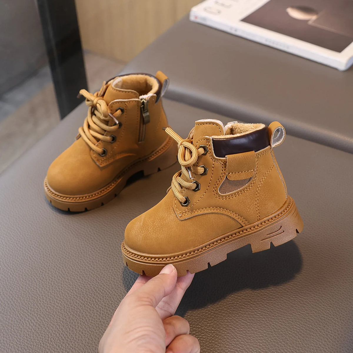 A close-up of a tan kids' winter leather boot with laces and a side zipper resting on a gray surface.