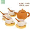 An orange silicone pretend play tea set with a teapot and four cups on yellow saucers.