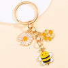 Gold-toned enamel keychain featuring a daisy flower and a bee charm.