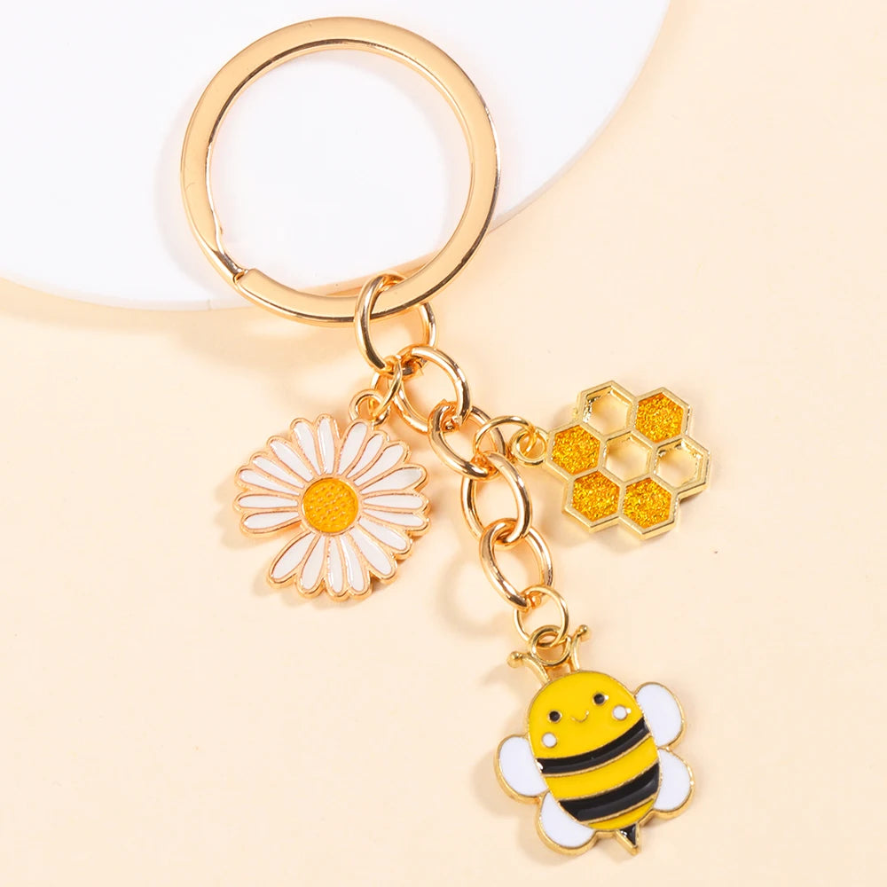 Gold-toned enamel keychain featuring a daisy flower and a bee charm.