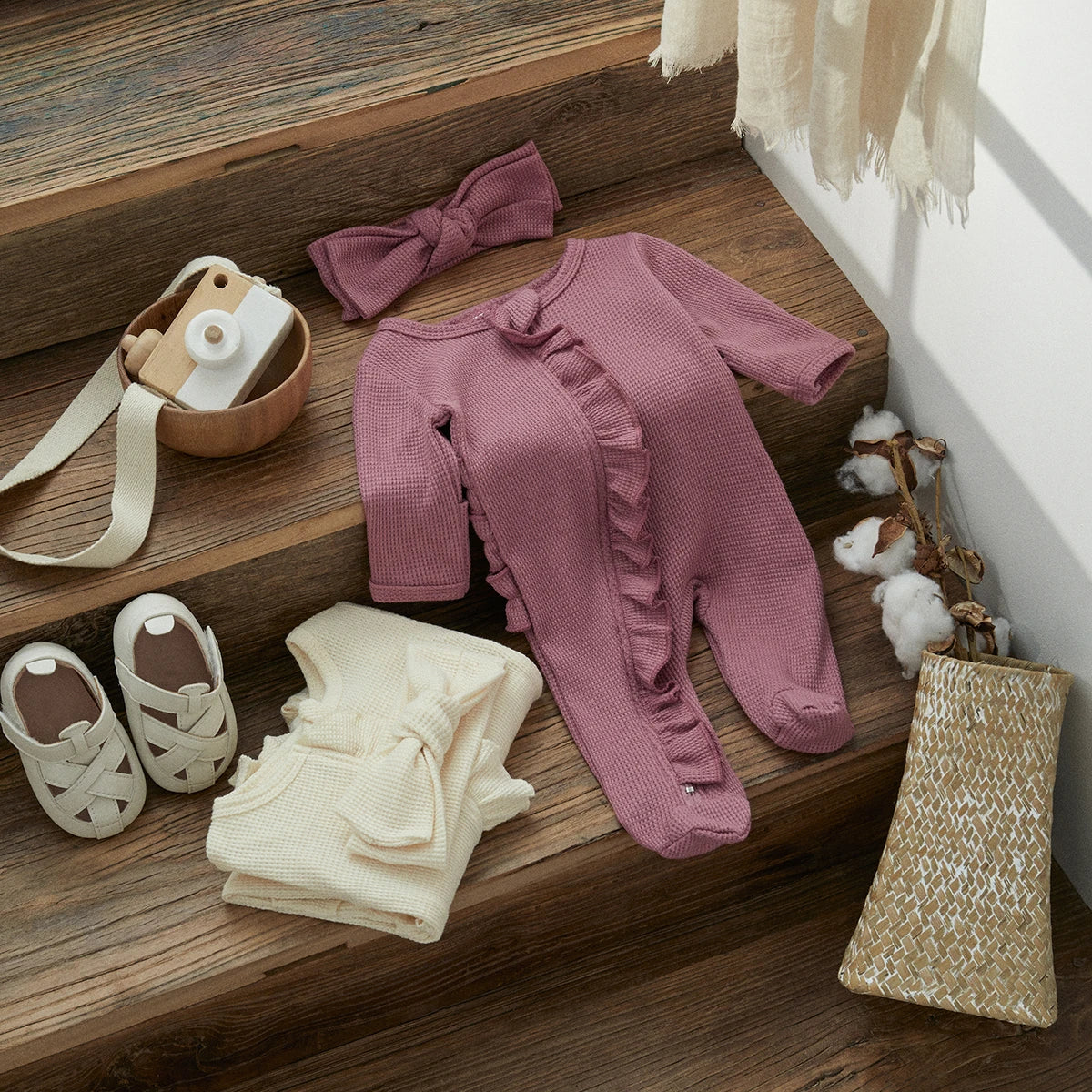 A pink knit ruffle romper and matching headband displayed on a wooden surface.
