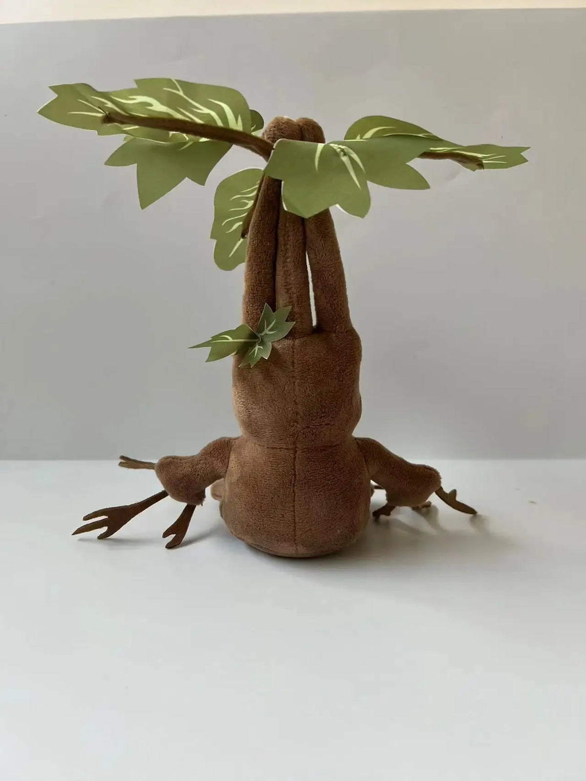 A brown plush toy resembling a mandrake with green leaves growing from its head.