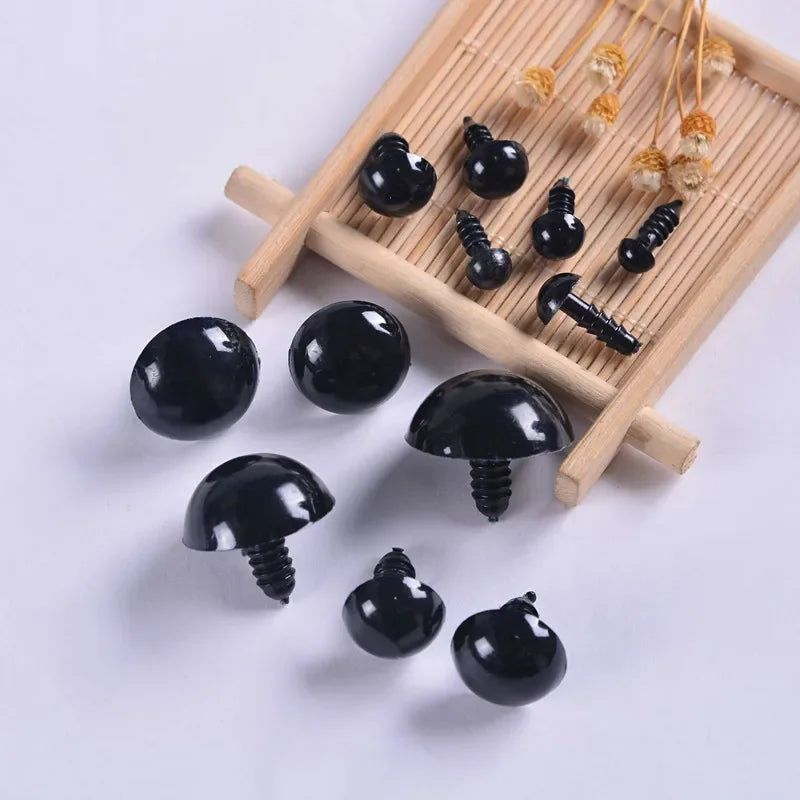 A collection of black plastic safety eyes in various sizes and styles arranged on a wooden tray.