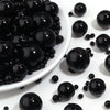 A close-up view of small, round black imitation pearl beads scattered on a white surface.