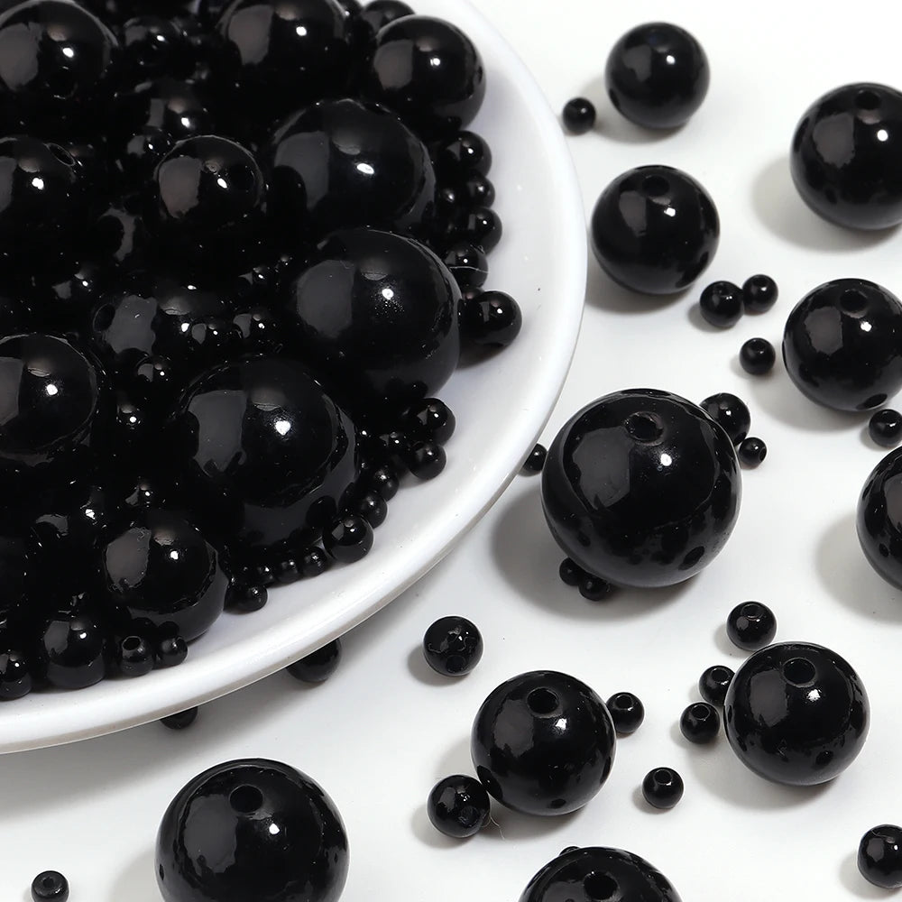 A close-up view of small, round black imitation pearl beads scattered on a white surface.