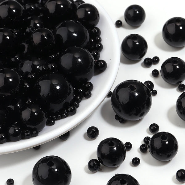 Gros plan de petites perles noires imitation, rondes, éparpillées sur une surface blanche.