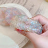A hand holds a cluster of translucent, iridescent squishy stress relief balls in various pastel shades.