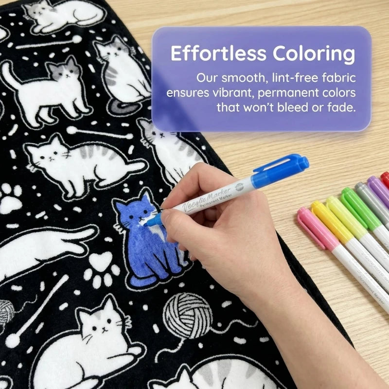 A hand colors a black cat design on a dark blanket using blue markers, demonstrating effortless coloring.