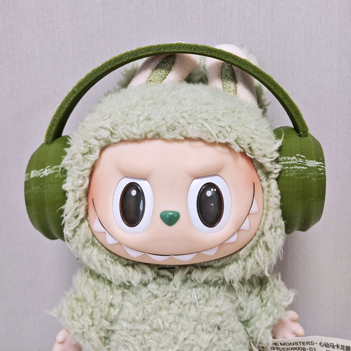 Labubu doll wearing a green fuzzy hoodie and headphones.