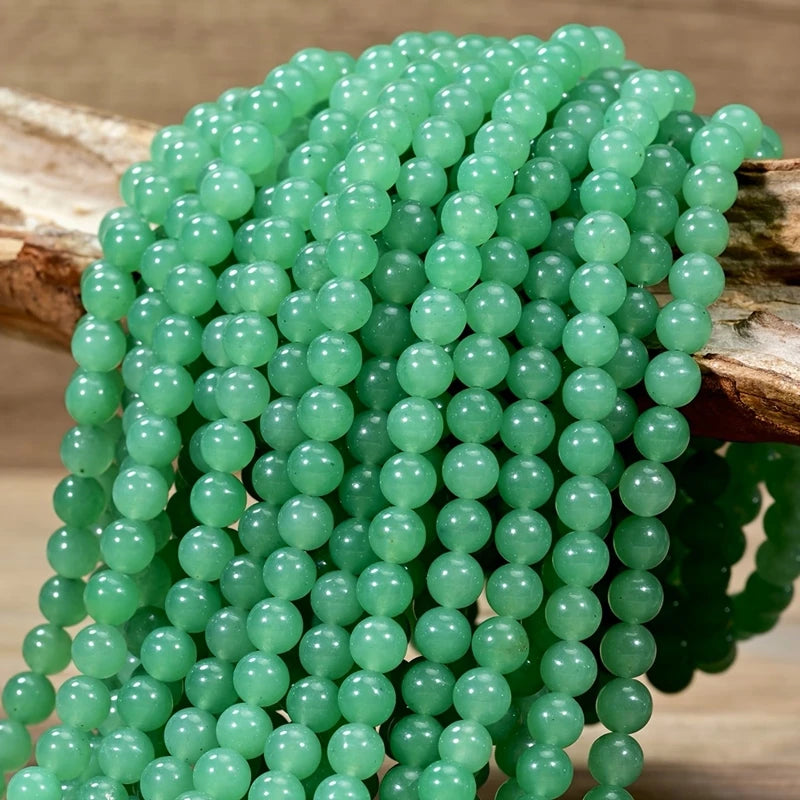 A strand of translucent green Aventurine gemstone beads is displayed on a wooden stick.
