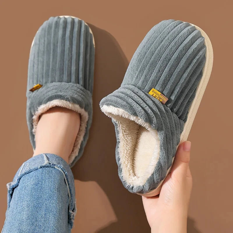 A pair of gray faux fur slippers being held, showing the plush lining and textured exterior.