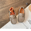 A pair of taupe slip-on moccasins with orange lining and bow details resting on a white cloth.