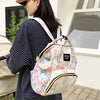 A woman holds a pink cartoon print waterproof diaper bag with yellow trim in an outdoor setting.
