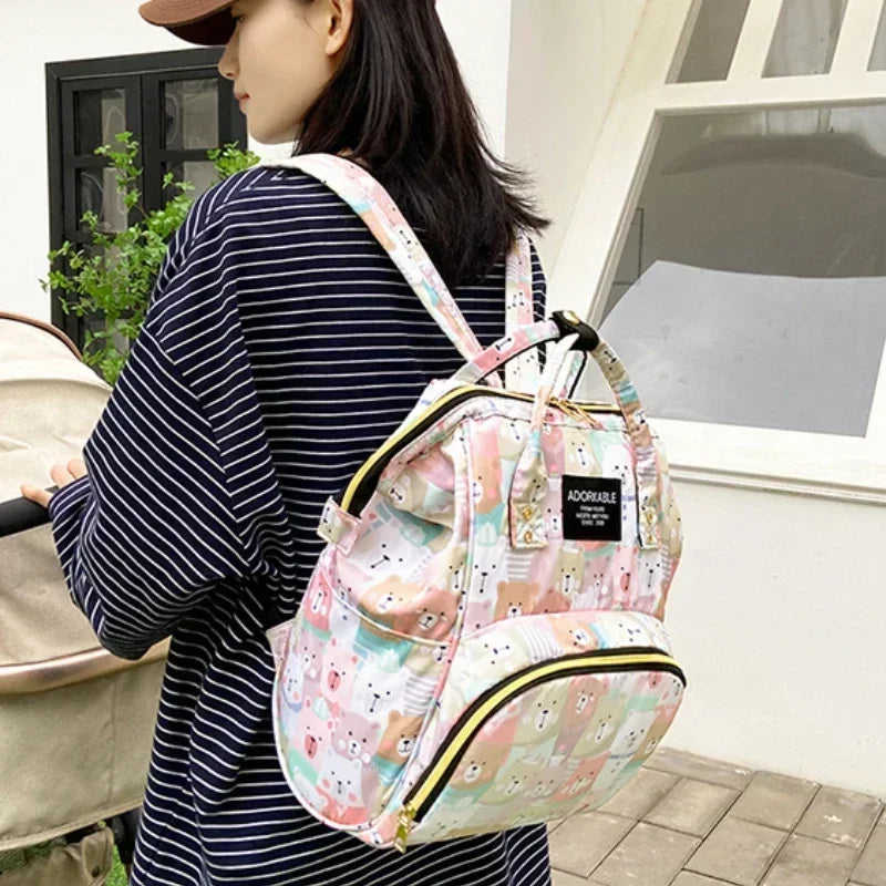 A woman holds a pink cartoon print waterproof diaper bag with yellow trim in an outdoor setting.