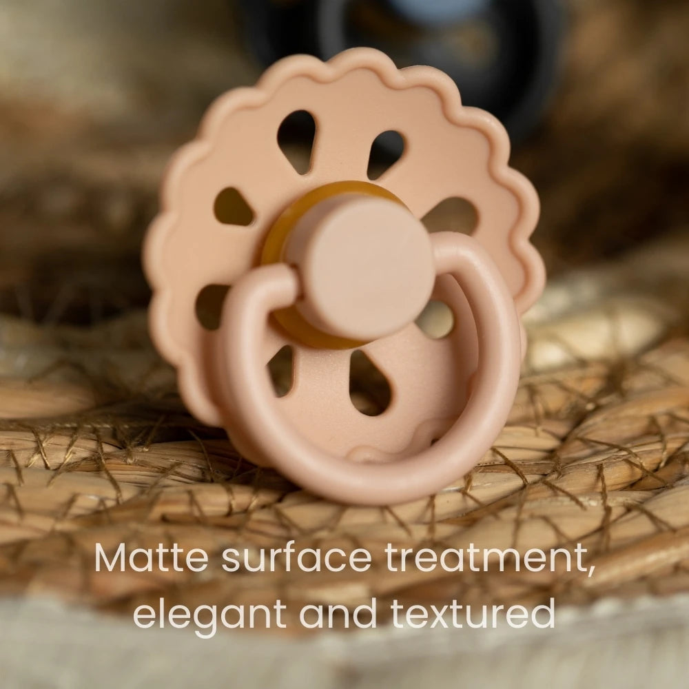 A light beige natural latex baby pacifier with a textured surface resting on a woven background.