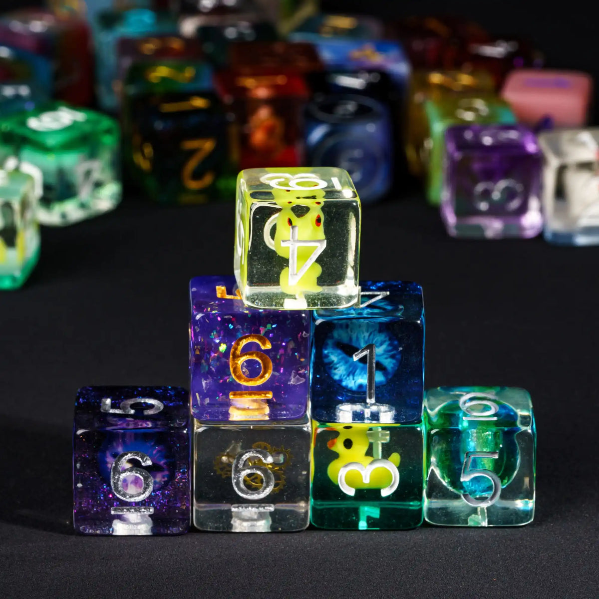 A collection of seven polyhedral resin dice in various colors and sizes arranged on a dark surface.