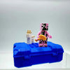 A pink and black Minecraft Steve figure stands on a blue box with white accessories.