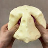 A hand is holding a pale yellow cheese wedge squishy stress relief toy.