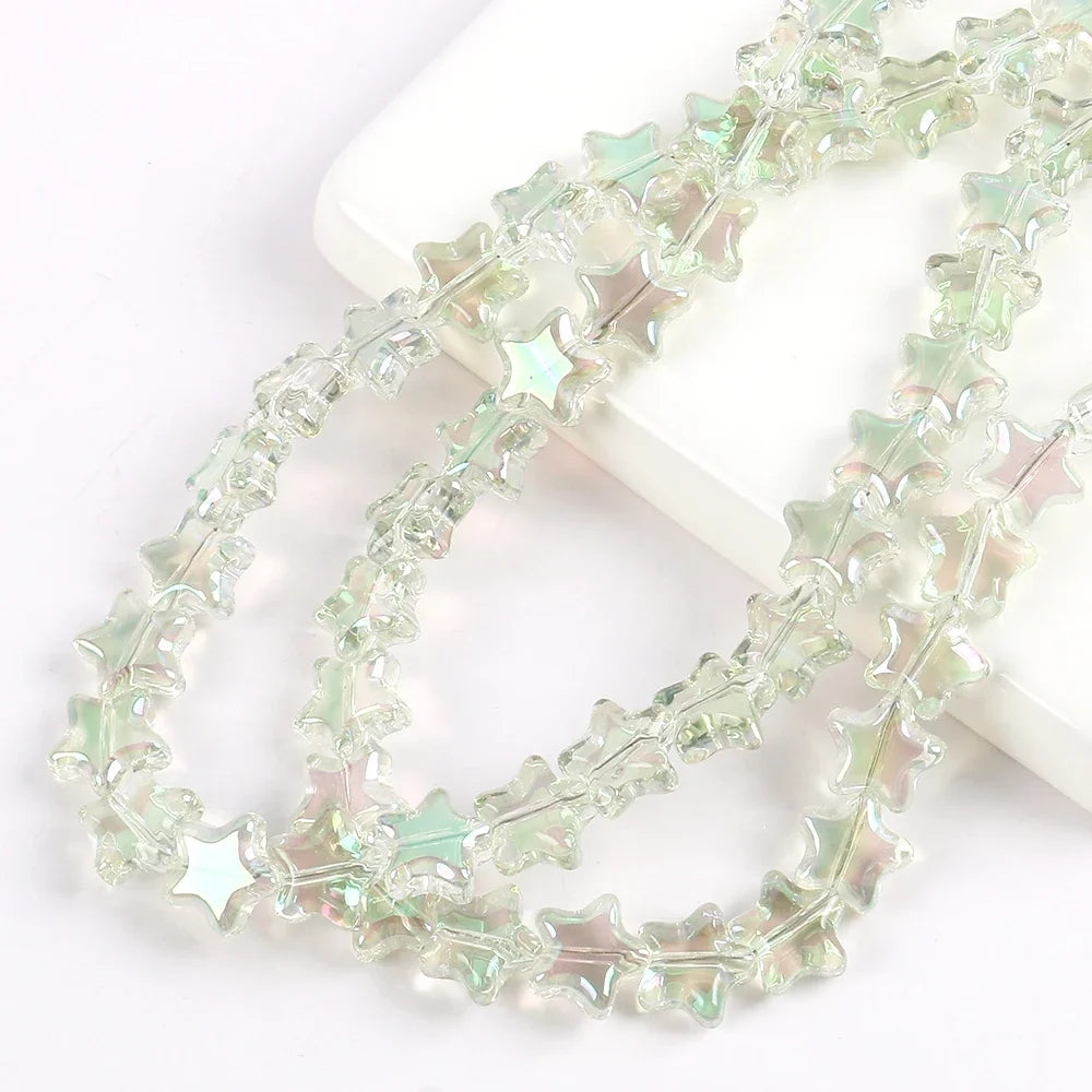 A strand of clear green glass star spacer beads for jewelry making laid out on a white surface.