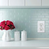 A white ceramic vase with pink roses sits on a light countertop in front of a light blue tiled wall featuring a white electri