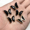 Gold-toned butterfly charm beads with black enamel and clear crystal accents displayed on a hand.