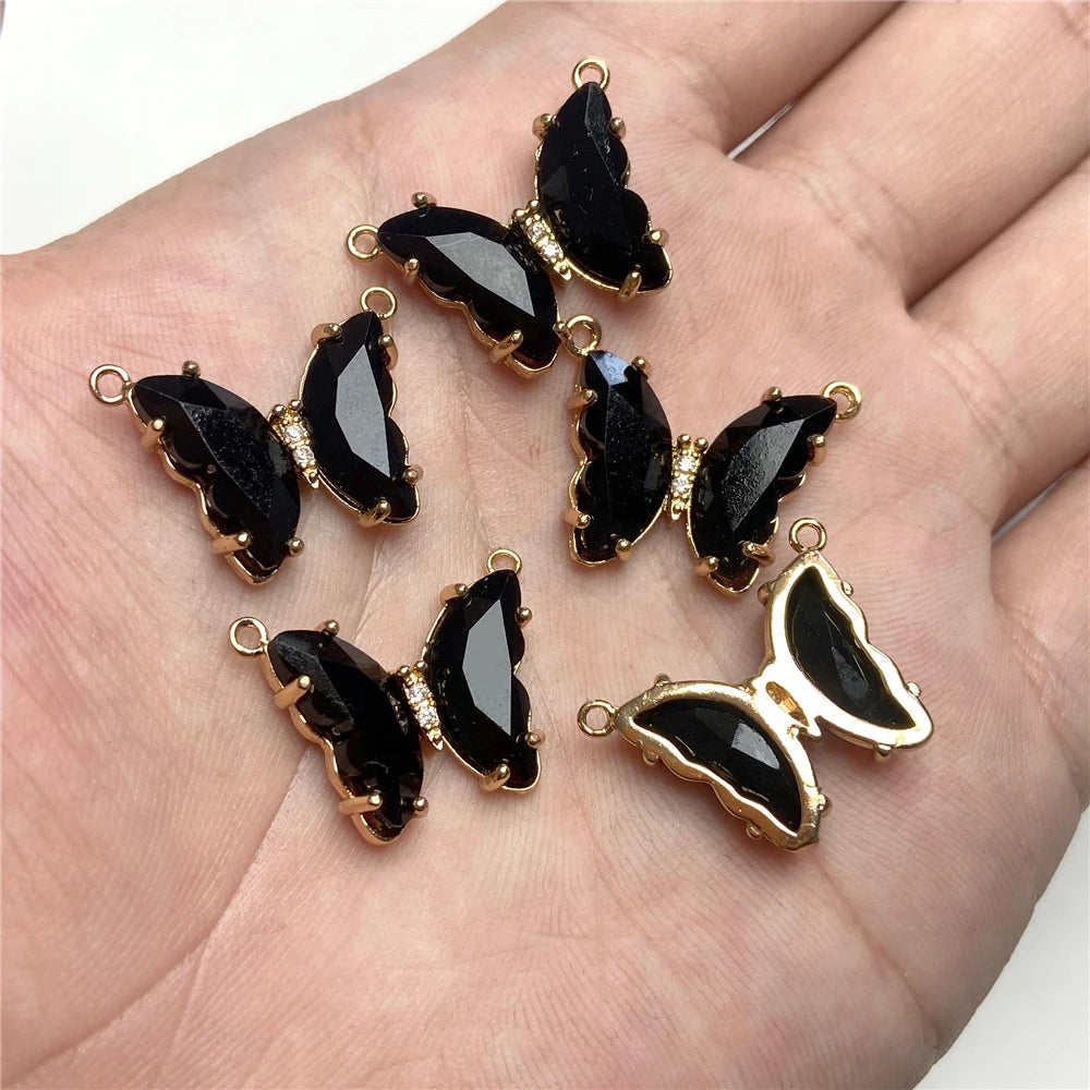 Gold-toned butterfly charm beads with black enamel and clear crystal accents displayed on a hand.